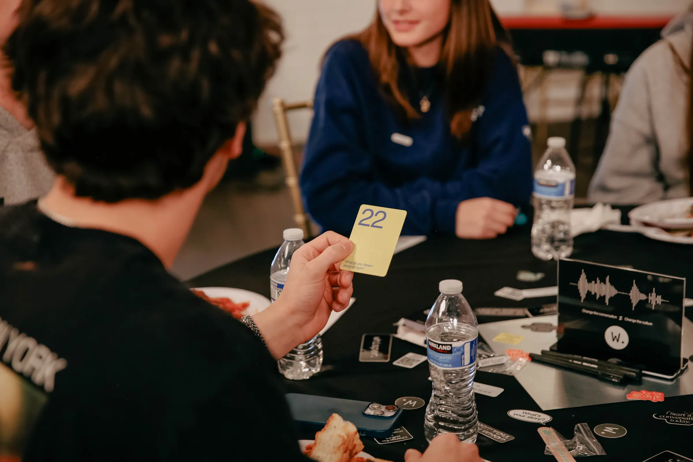 Two students speaking in front of a “Change the conversation” banner while others listen at their tables
